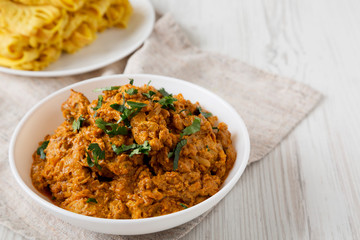 Homemade Chicken Tikka Masala in a white bowl on a white wooden background, low angle view. Space for text.