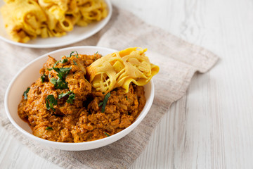 Homemade Chicken Tikka Masala in a white bowl on a white wooden background, low angle view. Copy space.