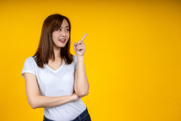 Young elegant Asian woman smiling and pointing to empty copy space isolated on yellow background