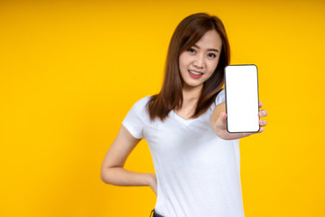 Naklejka premium Smiling young Asian woman is showing a smartphone standing on yellow background.