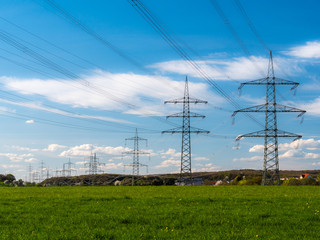 Pylons of a  high-voltage power lines against the blue sky with clouds on a green field. Electrical industry.