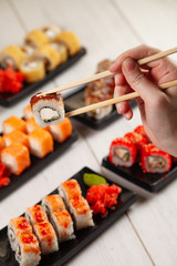 Hand holds chinese chopsticks with sushi on food background