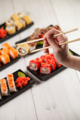 Hand holds chinese chopsticks with sushi on food background