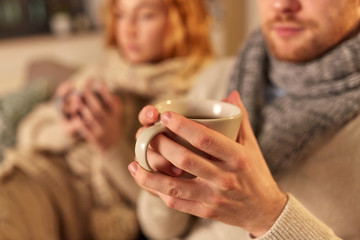 health, flu and people concept - close up of sick young couple in scarves drinking hot tea at home