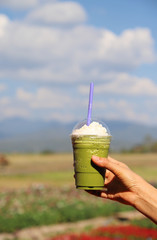 Closeup of woman's hand showing  a cup of  cold green tea smoothie with natural background. Vertical view.