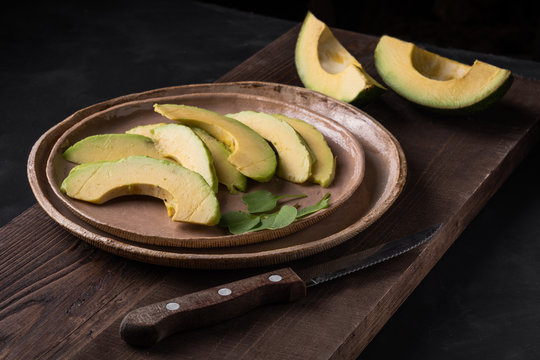 Sliced Avocado On A Plate On Wooden Boards In Low Key