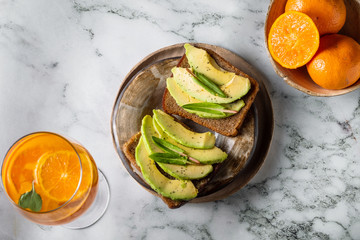 sandwiches with avocado on a plate with oranges and cocktail on a marble background
