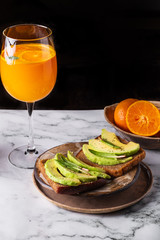 Fototapeta na wymiar sandwiches with avocado on a plate with oranges and cocktail on a marble background