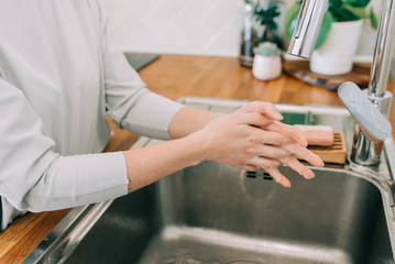 Hygiene to stop spreading coronavirus. Woman washing hands rubbing with soap in sink in kitchen.