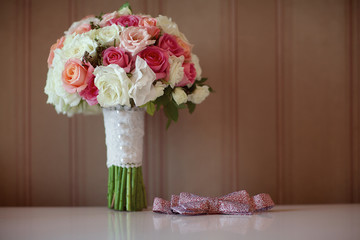 Fresh wedding bouquet with roses stands on white table next to pink bow tie