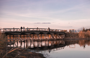 People fishing on an old wooden bridge at sunset