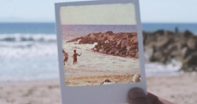 Polaroid frame held up to camera revealing vintage footage of people playing and frolicking at beach
