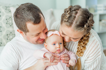 Beautiful young parents are holding their little newborn daughter in their arms. Blue-eyed little girl of 2 months. Baby