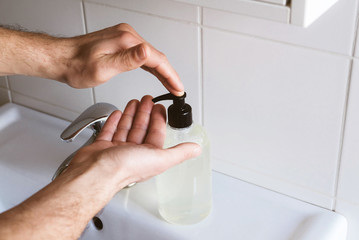 Man cleaning his hands using liquid disinfectant soap and water in bathroom.