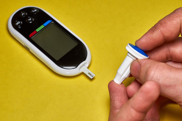 A diabetic checks his blood sugar. Close up man hands self-tested with a Lancet and a glucometer at home.