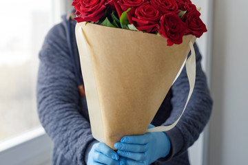 contactless flower delivery, male courier in a protective face mask, medical gloves with a bouquet of red roses, the concept of the decline of the flower business