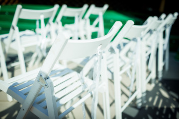 White folding wooden chairs Terje stand in a row outdoors. Wedding ceremony