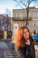 Fototapeta na wymiar A brunette girl with long hair in a jacket stands on a bridge with statues of white lions in the middle of the canals of St. Petersburg, Attractions, morning spring