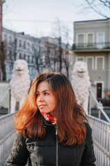 A brunette girl with long hair in a jacket stands on a bridge with statues of white lions in the middle of the canals of St. Petersburg, Attractions, morning spring