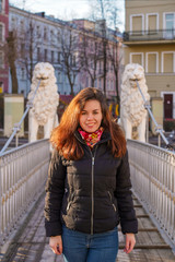 A brunette girl with long hair in a jacket stands on a bridge with statues of white lions in the middle of the canals of St. Petersburg, Attractions, morning spring