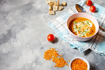 Delicious lentils soup with heavy cream on concrete table with red bell pepper, bread toasts.