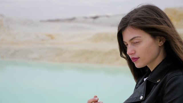 Portrait of a brunette girl in a black jacket looking at the camera, against a background of sand quarry, close-up. Slow motion.