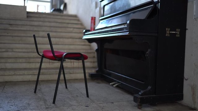 Old black piano on the street with broken chair nearby. Retro piano with open cover staying near the marble stairs, abandoned musical instrument outdoors