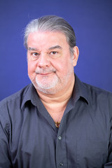 Man studio closeup portrait. He is serious and looking to the camera. His face shows some disappointment around him. The background is lighted with blue color.