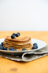 Homemade pancakes arranged on a white plate with blueberries on the table - Copy space