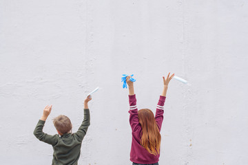 a boy and a girl stand against a white wall and having fun of the end of quarantine due to the coronavirus pandemic, children with protective masks and gloves in their hands