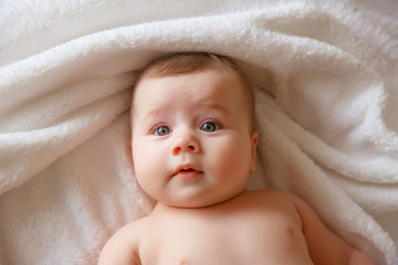 baby is wearing diapers and a white towel in bedroom. A newborn baby is resting in bed after a bath or shower. Children's room. Textiles and bedding for children.