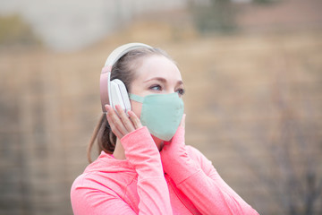 Young girl in a face mask and headphones walking in the park. The new recommendation - everyone to wear masks in public during the coronavirus covid-19 pandemic.