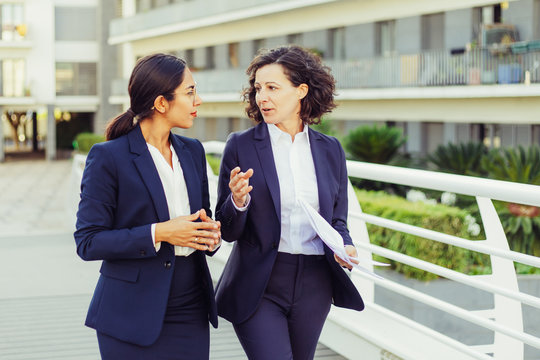 Focused Female Professionals Discussing Project On Their Way To Office. Business Women Walking Outside In City. Corporate Communication Concept