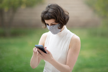 A white woman in a fabric face mask while using her phone. The new recommendation -everyone to wear masks in public during the coronavirus pandemic.