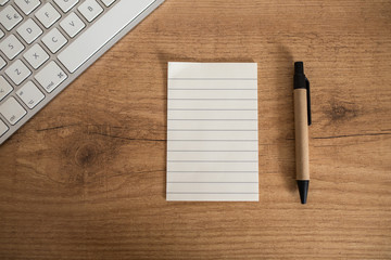 Flat lay, top view office rustic table wooden desk. Workspace with keyboard, scratch pad and pen. Work from home. Copy space.