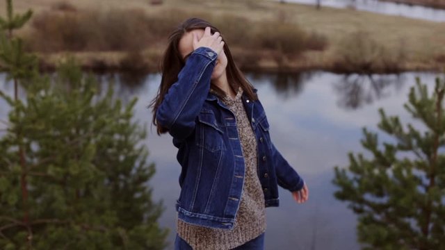Happy hipster female in casual clothes spinning and touching hair while walking in nature along picturesque river in slow motion