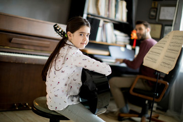 Little girl playing guitar with her music teacher in the rustic apartment