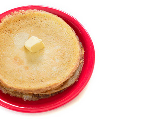 Staple of wheat golden yeast pancakes or crepes on red plate on a white background closeup