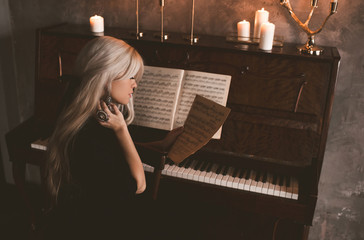 Beautiful blonde girl playing piano with candles in room closeup. Romantic mood. Social isolation....