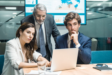 Naklejka premium Front view of confident business team working at office. Group of office employees sitting at table and working over new project. Business, teamwork concept
