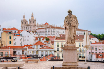  Statue at Santa Luzia viewpoint, with St. Vincent Church in the background in Lisbon, Portugal.