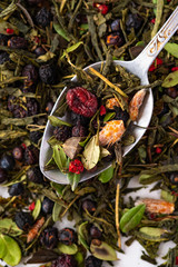Dried organic green tea with berries and forest herbs on a teaspoon, top view