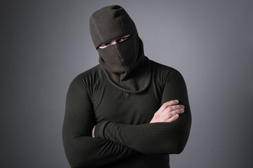 A man in a balaclava, as a concept of special forces clothing, stands with a menacing look, clasped hands on his chest.