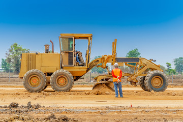 Motor grader clearing and leveling construction site surface while worker controlling level point....