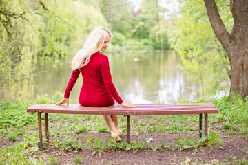 Blond woman wearing an office clothes sitting on a bench in the park near a lake. The picture reflects the return to natural life.