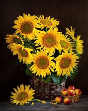still life of sunflower flowers in a wicker basket on the table, dark background. Peaches on a plate.