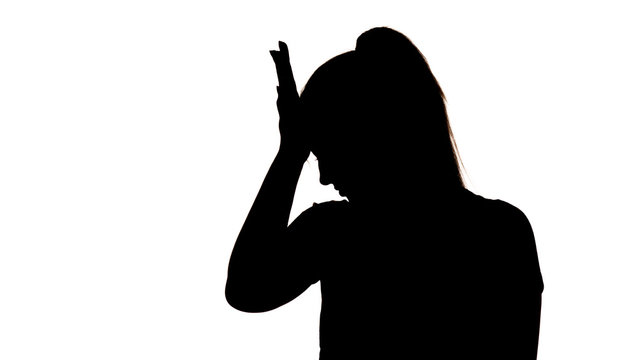silhouette of a young frustrated woman with hand near forehead on a white isolated background, concept female emotions, fear and depression