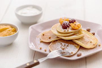 vegetarian pancakes with honey, raspberries and physalis, sprinkled with powdered sugar with sour cream and jam on white background