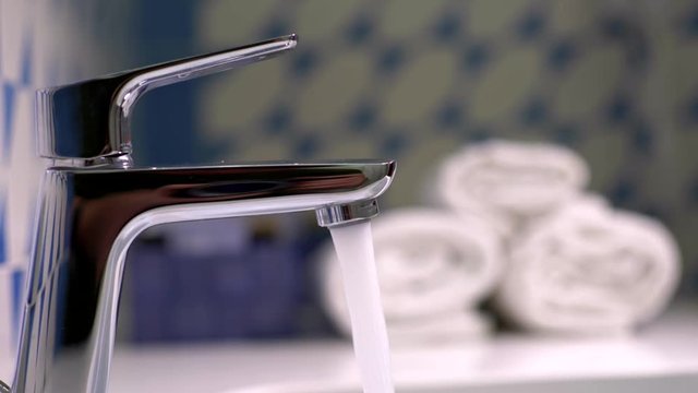 Water flowing from a shiny chrome plated water tap. Slow motion shot
