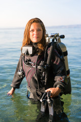 Female Scuba Diving Instructor Standing in Water Wearing a Dry Suit, a Twin Tank and Holding Fins